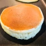 Cooked almond flour pancake on griddle. Second pancake in the background waits to be flipped.