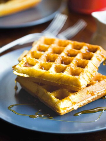 Two almond flour waffles on a plate with syrup.