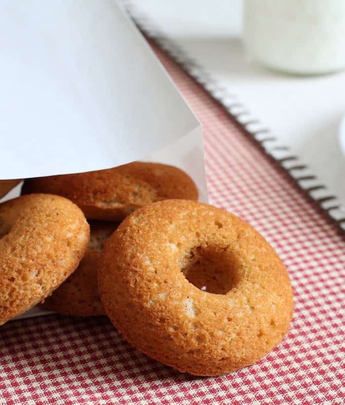 Paleo doughnuts coming out of a bakery bag onto a red checkered tablecloth.