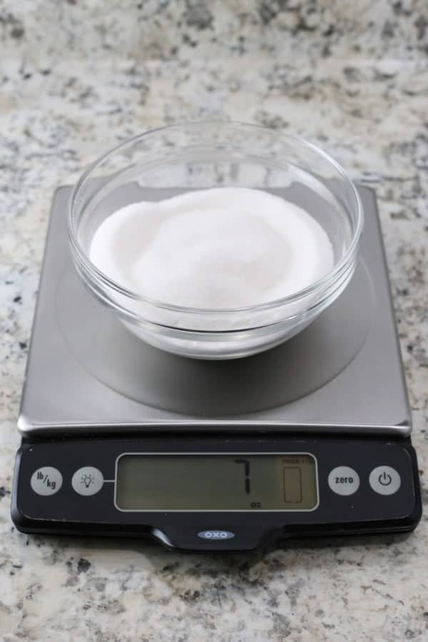 Granulated sugar in glass bowl on digital scale. Display reads 7 ounces.