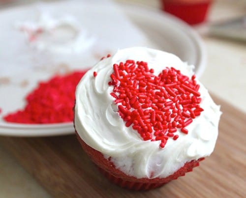 Cupcake with white frosting and red sprinkle hearts.