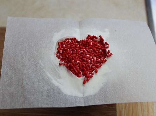 Red sprinkles in paper template on top of frosted cupcake.