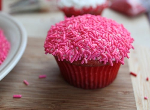 Gluten-free cupcake topped with frosting and covered with pink sprinkles.