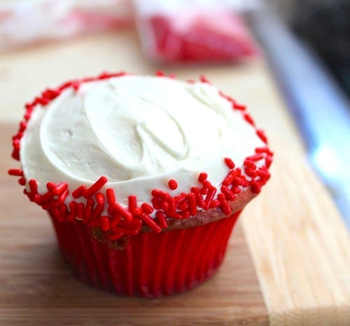 White frosted cupcake with red sprinkles on the edge.