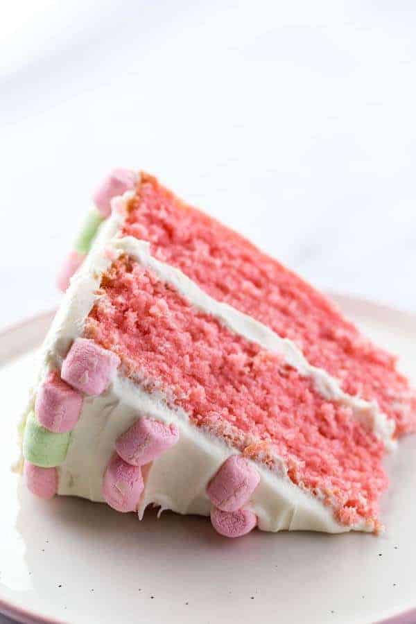 Gluten-Free Strawberry Cake Slice on Plate. Frosted with cream cheese frosting and decorated with pink and green marshmallows.