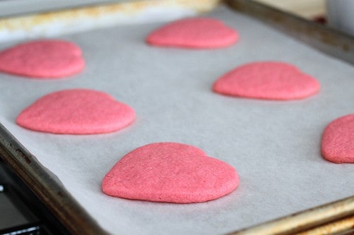 Pink gluten-free sugar cookie hearts cooling on a pan.