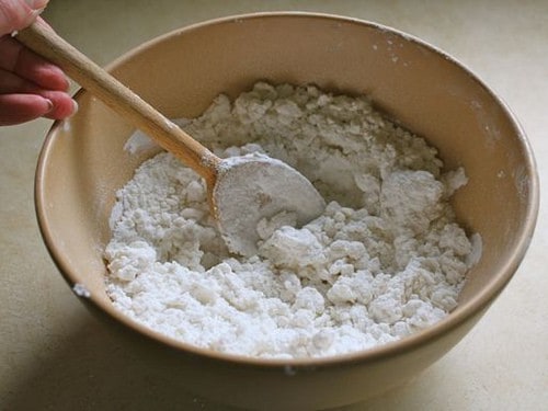 Gluten-free flour tortilla dough in mixing bowl with a wooden spoon. The mixture looks dry.