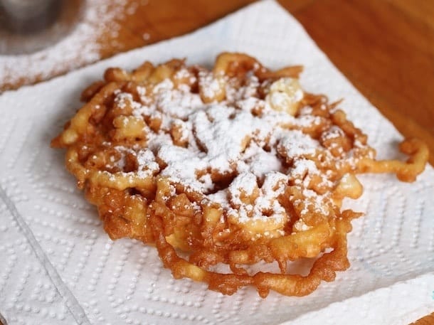 Gluten-free funnel cake dusted with powdered sugar on paper towel.