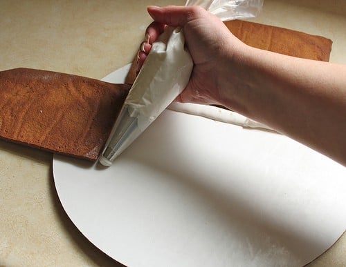 Piping frosting on white cardboard to secure a gluten-free gingerbread house.