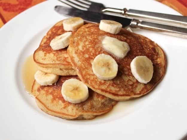 Gluten-Free Banana Pancakes on a plate, topped with syrup and banana slices.