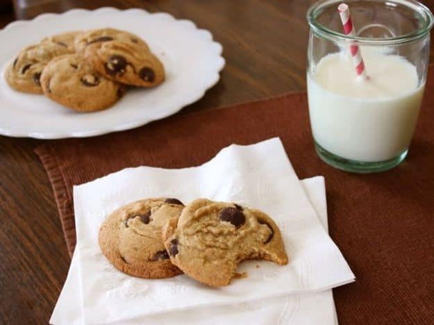 Gluten-free brown butter chocolate chip cookies on a napkin. A glass of milk and a platter of cookies is in the background.