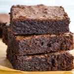 Stack of gluten-free brownies on a brown piece of parchment paper.