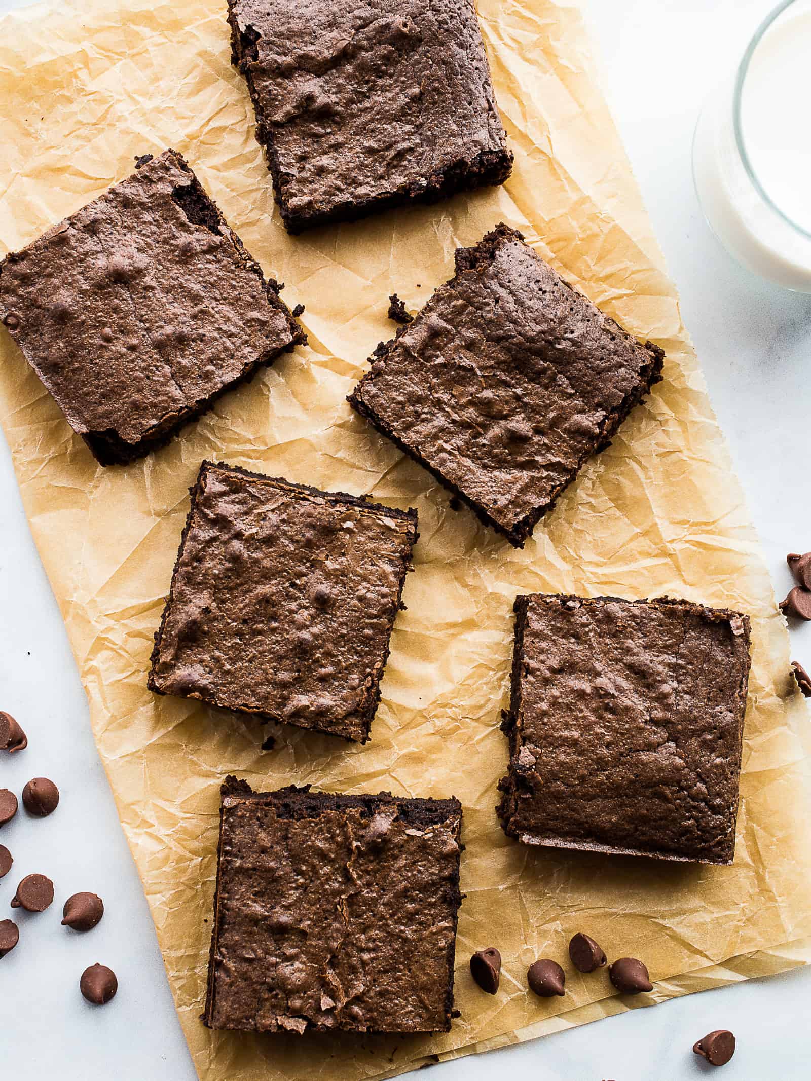 Gluten-free brownies on a piece of brown parchment paper. A glass of milk sits off to the right.