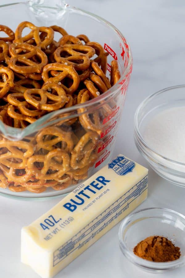 Measuring cup of pretzels. Stick of butter. Bowl of sugar. Small bowl of ground cinnamon.