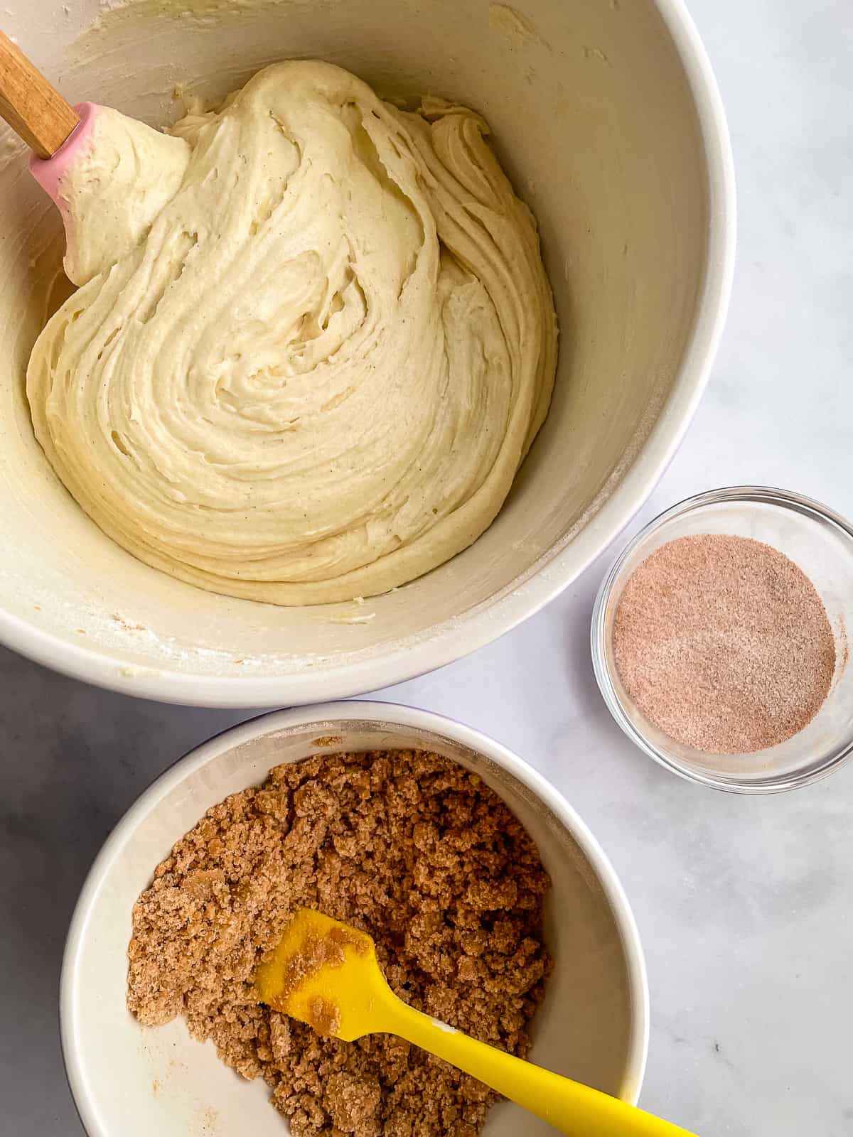 Bowl of gluten-free cake batter, crumb topping, and cinnamon sugar on the counter.