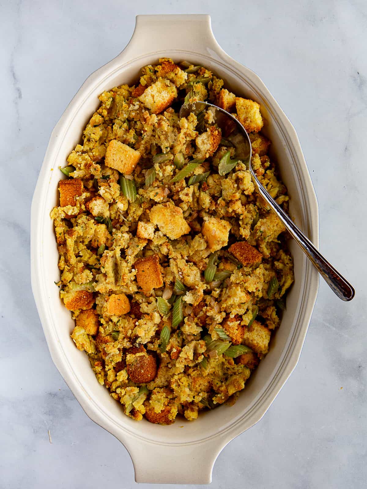 Gluten-free cornbread stuffing in an oval bowl with serving spoon.