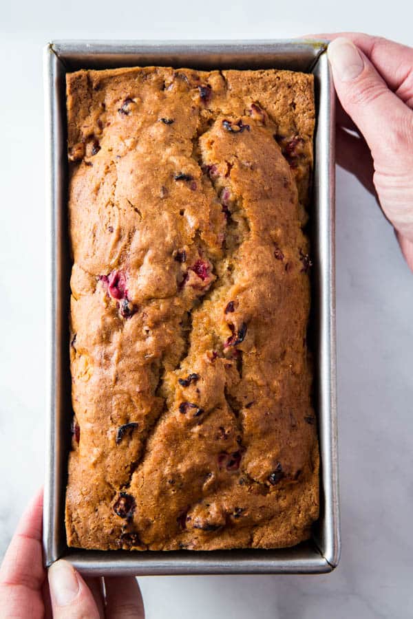 Baked gluten-free bread in pan. Two hands are lifting the pan.