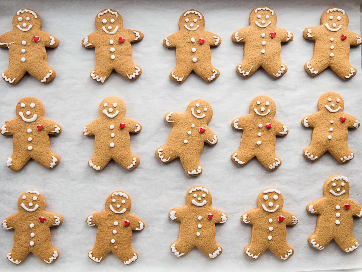 Gluten-free gingerbread cookies, decorated with faces and a small red heart, on a piece of parchment paper.