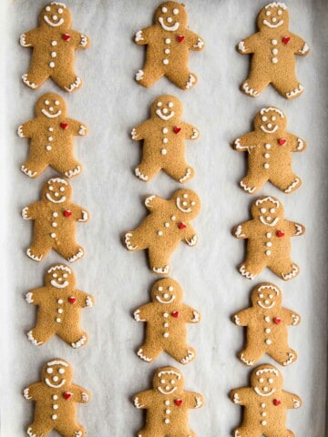 Gluten-free gingerbread cookies, decorated with faces and a small red heart, on a piece of parchment paper.