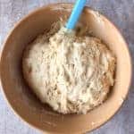 Bowl of gluten-free Italian Easter bread dough in wood bowl with blue spatula.