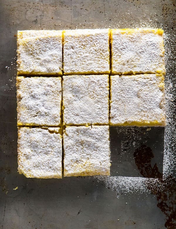 Gluten-free lemon bars topped with powdered sugar cut into nine squares. One bar is missing.