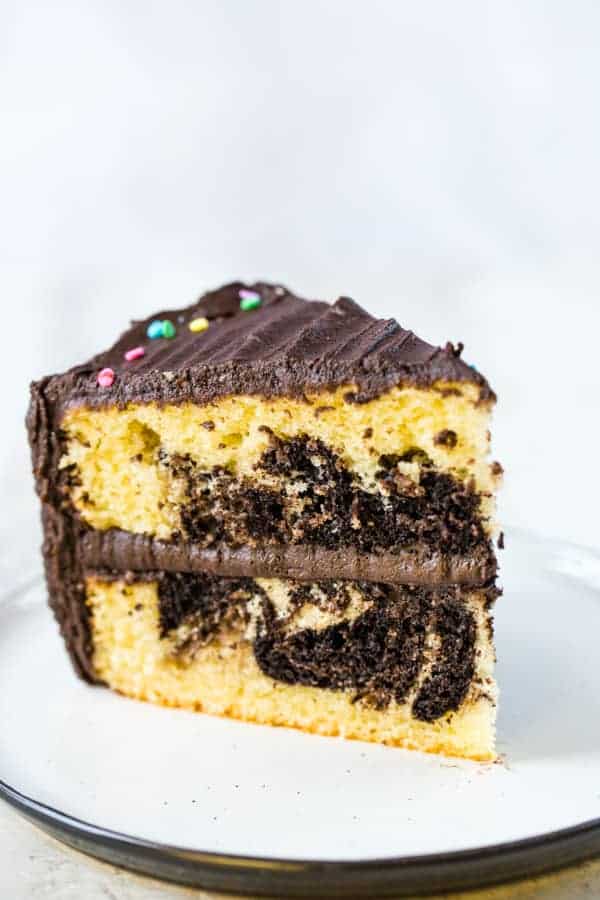 Slice of gluten-free marble cake, frosted with chocolate frosting, on a white plate.