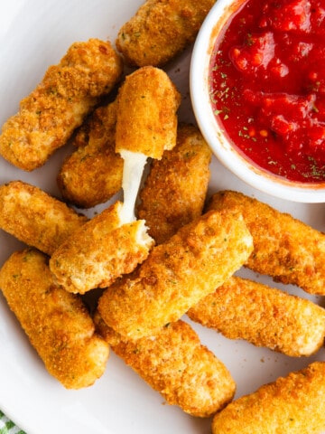 Gluten-free mozzarella sticks on a plate with a small bowl of tomato dipping sauce.