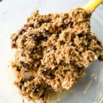 Gluten-free oatmeal cookie dough with chocolate chips in a glass bowl. A yellow spatula is in the bowl with the cookie dough.