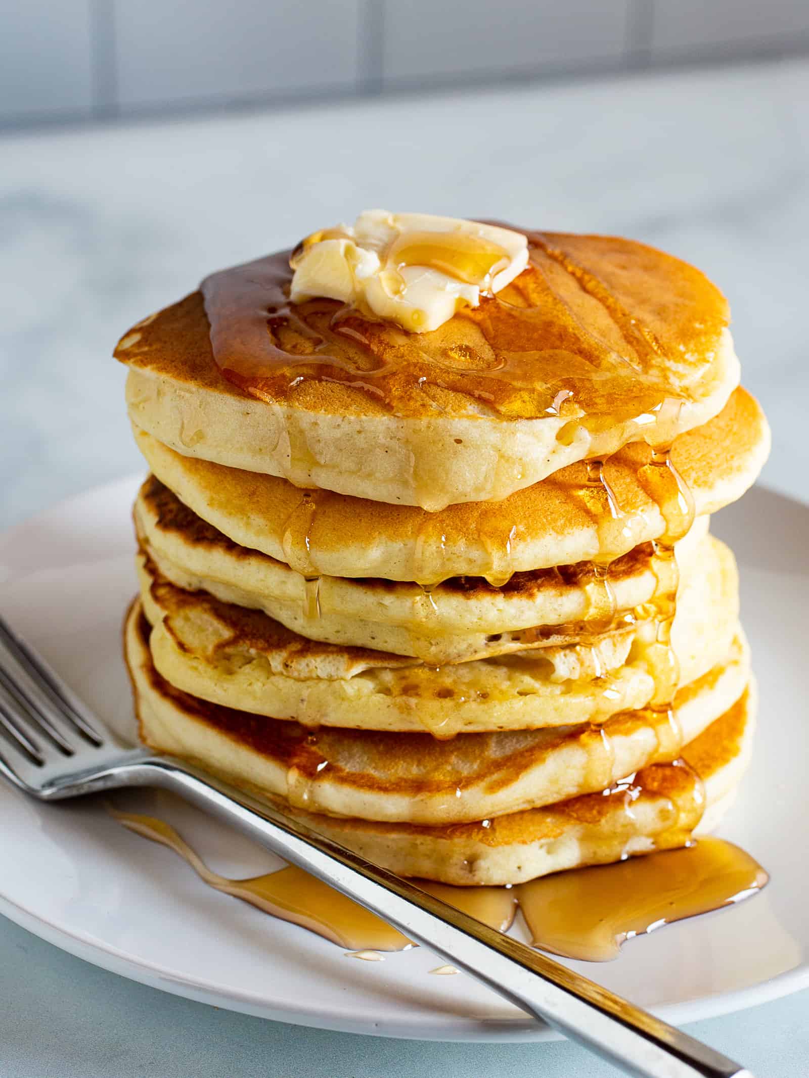 Stack of gluten-free pancakes on a plate with butter and syrup.