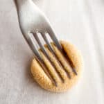 Fork pressing lines into a gluten-free peanut butter cookie.