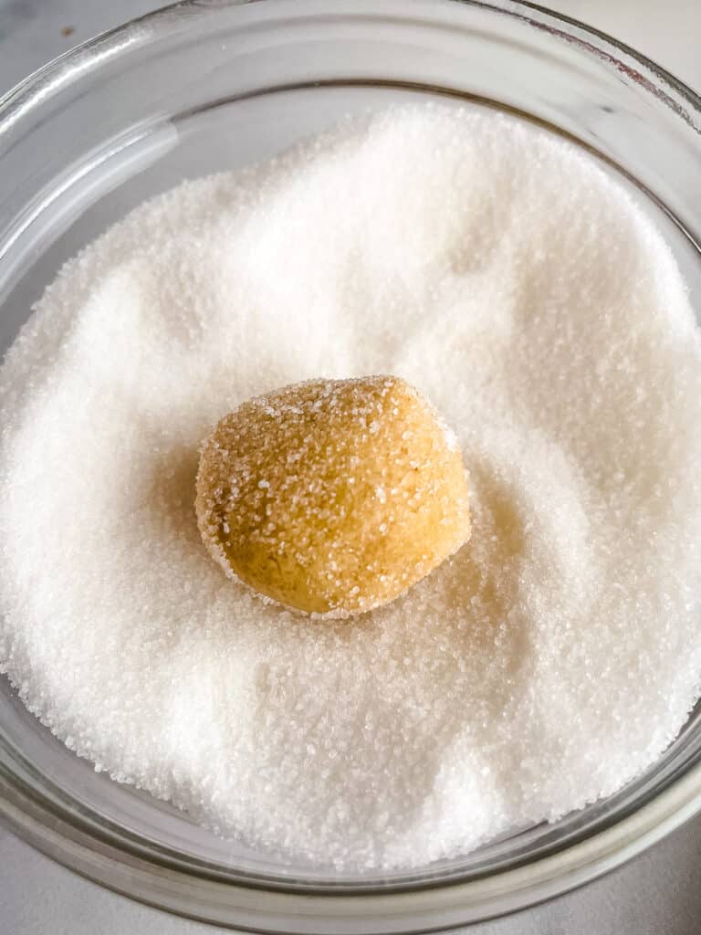 Gluten-free peanut butter dough being rolled in granulated sugar.