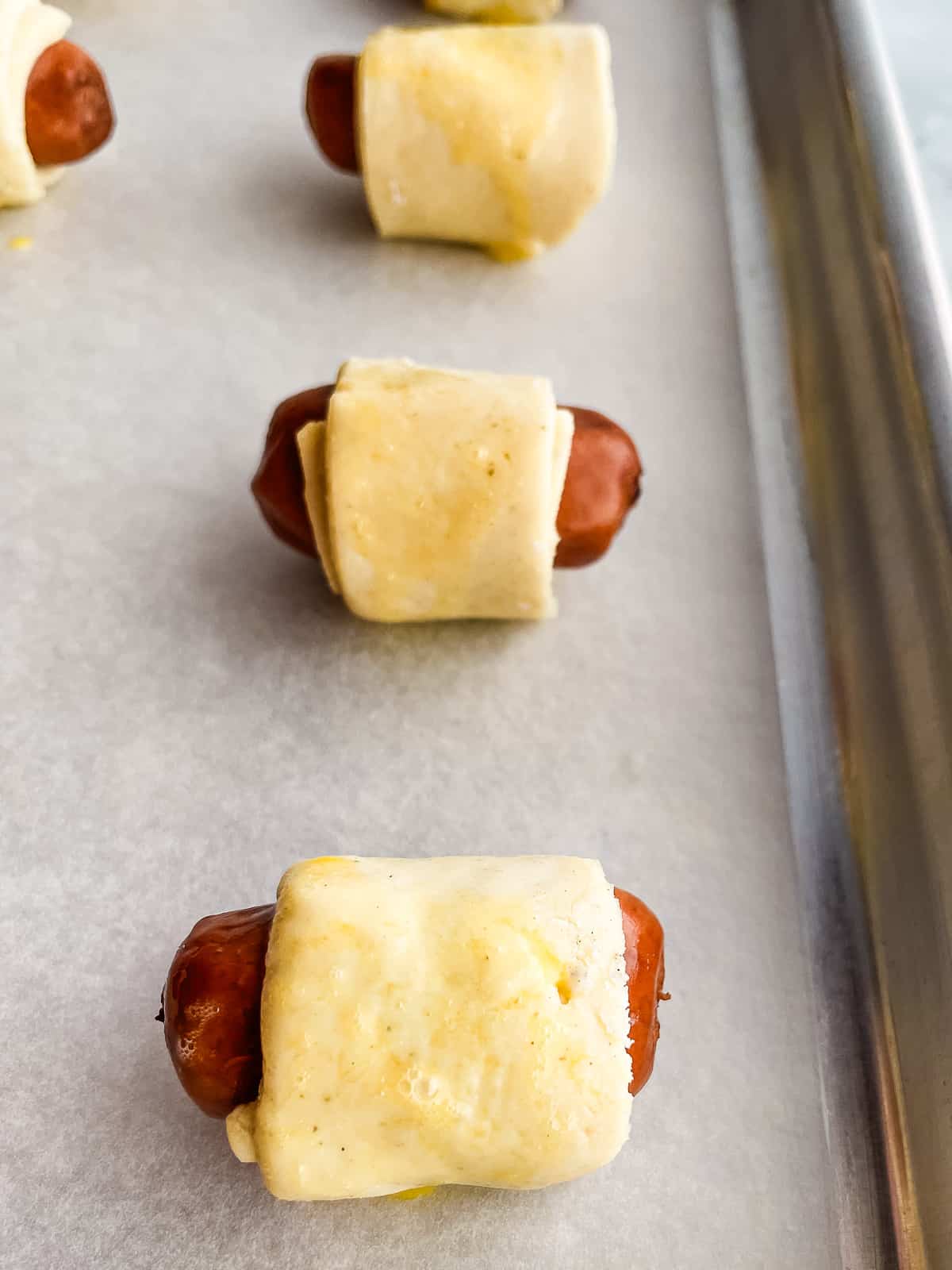 Unbaked gluten-free pigs in a blanket on a baking sheet.