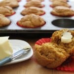 Gluten-Free Pumpkin Muffin split and spread with butter. Pan of muffins and stick of butter in background.