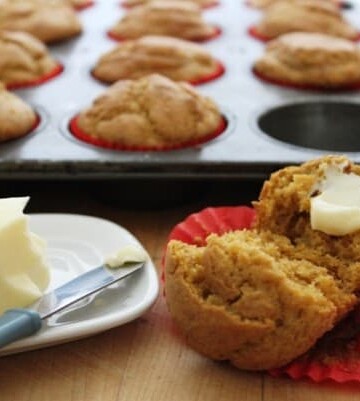 Gluten-Free Pumpkin Muffin split and spread with butter. Pan of muffins and stick of butter in background.