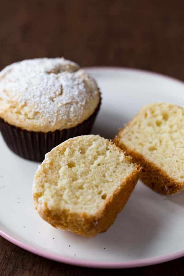 Gluten-free sour cream muffins topped with powdered sugar. One is split to show texture.