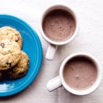 Dairy-free hot chocolate in two mugs. Small plate of chocolate chips on the left.