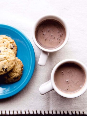 Dairy-free hot chocolate in two mugs. Small plate of chocolate chips on the left.