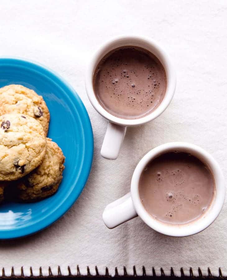 Dairy-free hot chocolate in two mugs. Small plate of chocolate chips on the left.