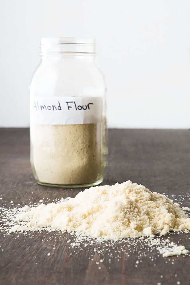 Jar filled with almond flour. A pile of almond flour sits in front of it.