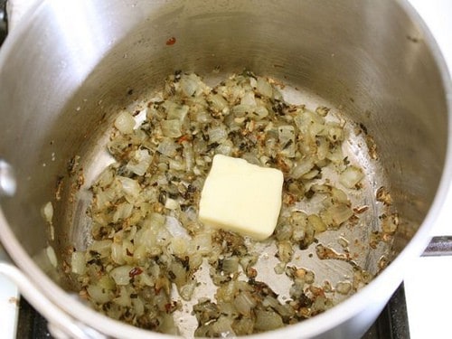 Pat of butter added to cooked onions, garlic, and herbs in a pot.