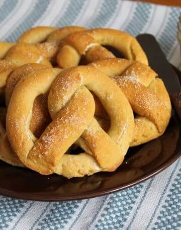 Gluten-free pretzels on a plate with a jar of mustard sitting to the right.