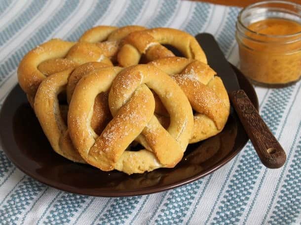 Gluten-free pretzels on a plate with a jar of mustard sitting to the right.