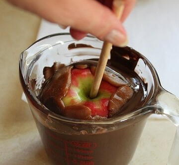 Dipping caramel coated apple in dark chocolate.