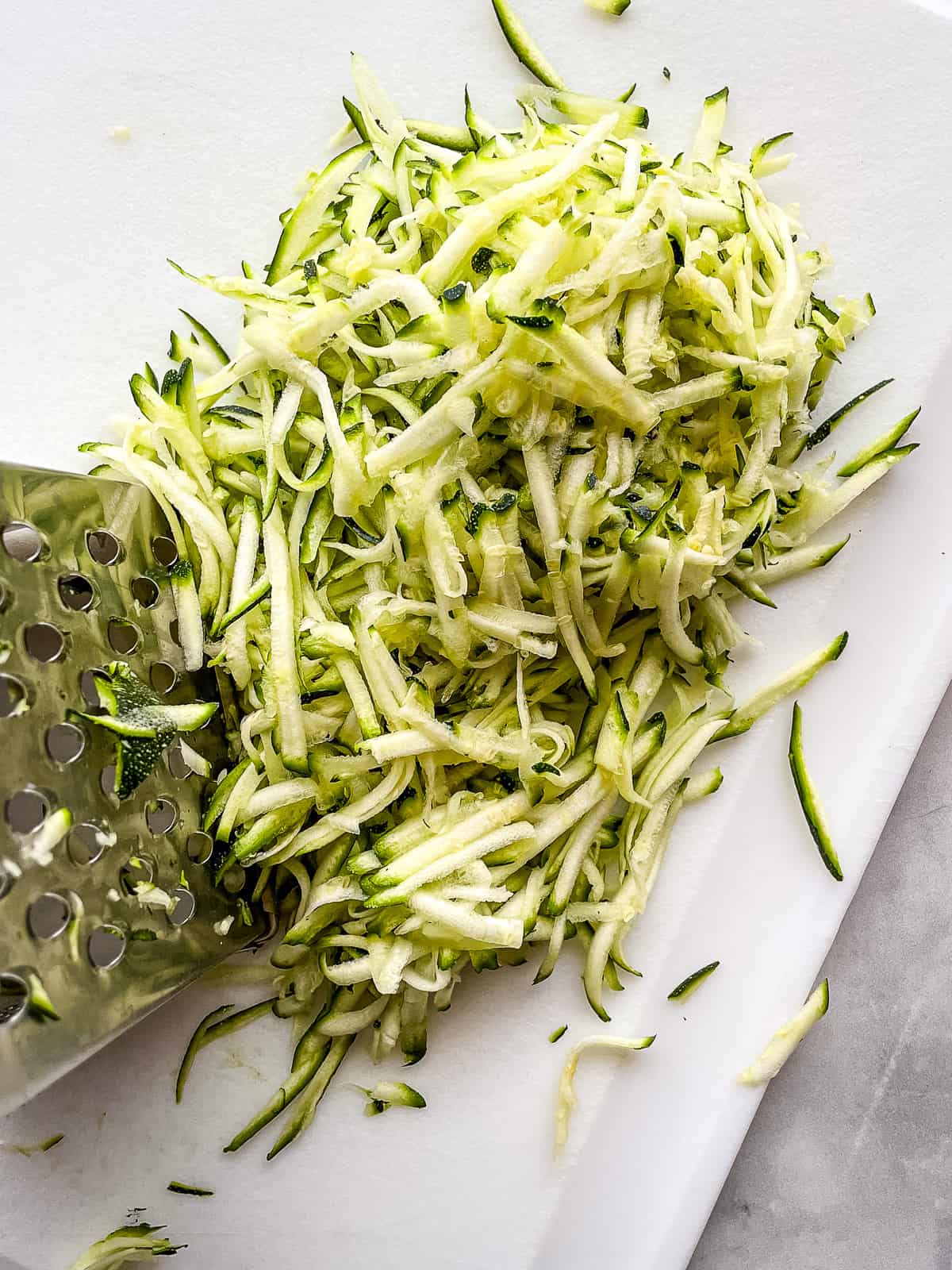 Shredded zucchini on a cutting board for gluten-free zucchini bread.