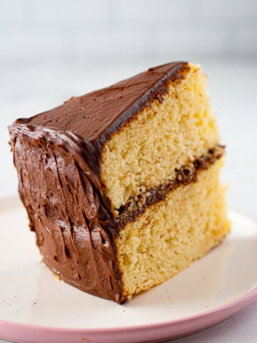 Slice of gluten-free chocolate cake with chocolate frosting on a plate.