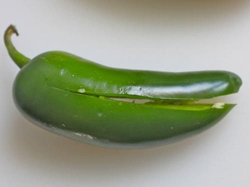 Sliced jalapeño pepper on a white cutting board.