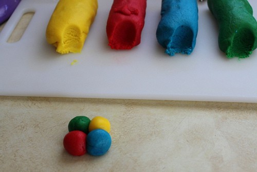 Yellow, red, blue, and green logs of gluten-free cookie dough. Four balls are together to make one cookie.