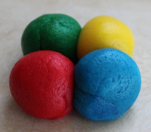 Green, yellow, blue, and red balls of gluten-free cookie dough.